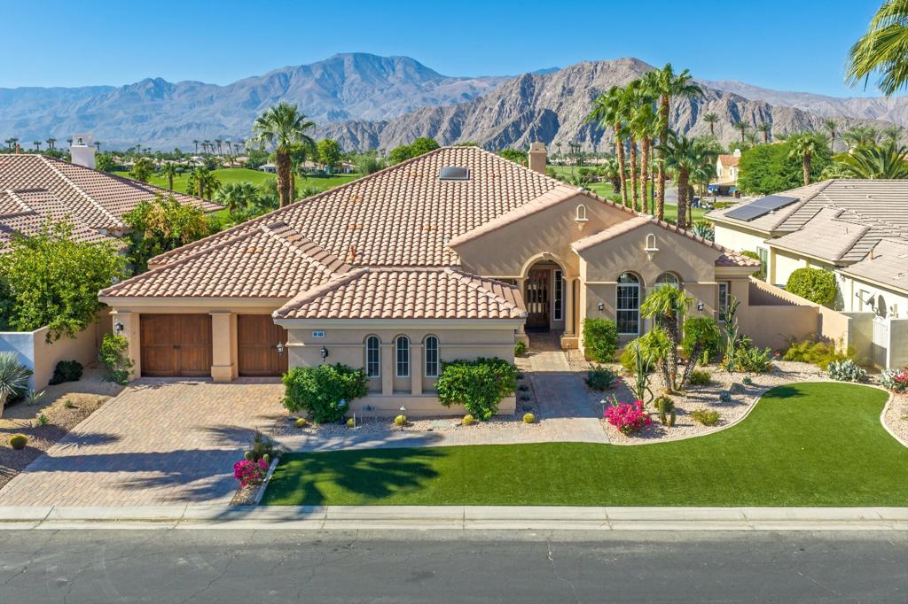 Tan stucco home with a tiled roof, landscaped lawn, and desert mountains behind it.