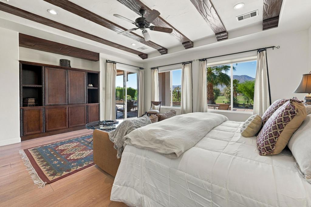 Bedroom with dark wood ceiling beams, built-in cabinetry, and views of landscaped grounds and mountains.