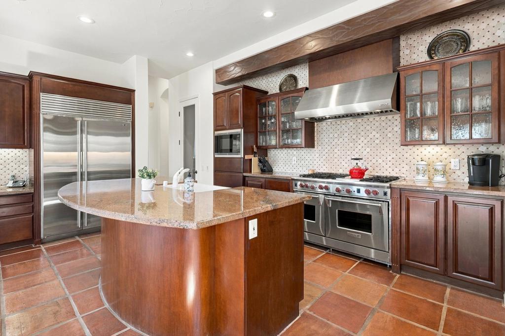 Kitchen with a rounded granite island, dark wood cabinetry, and stainless steel appliances.