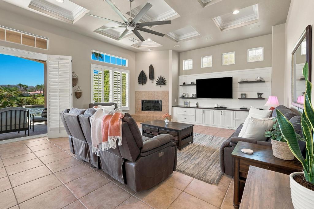 Furnished living room with coffered ceiling, built-in media wall, and open patio doors.