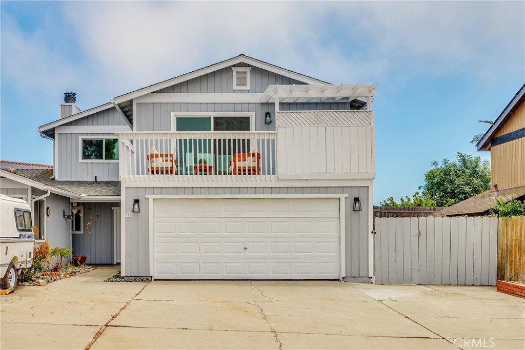 Gray two-story house with a white double garage, upper balcony, and broad concrete driveway.