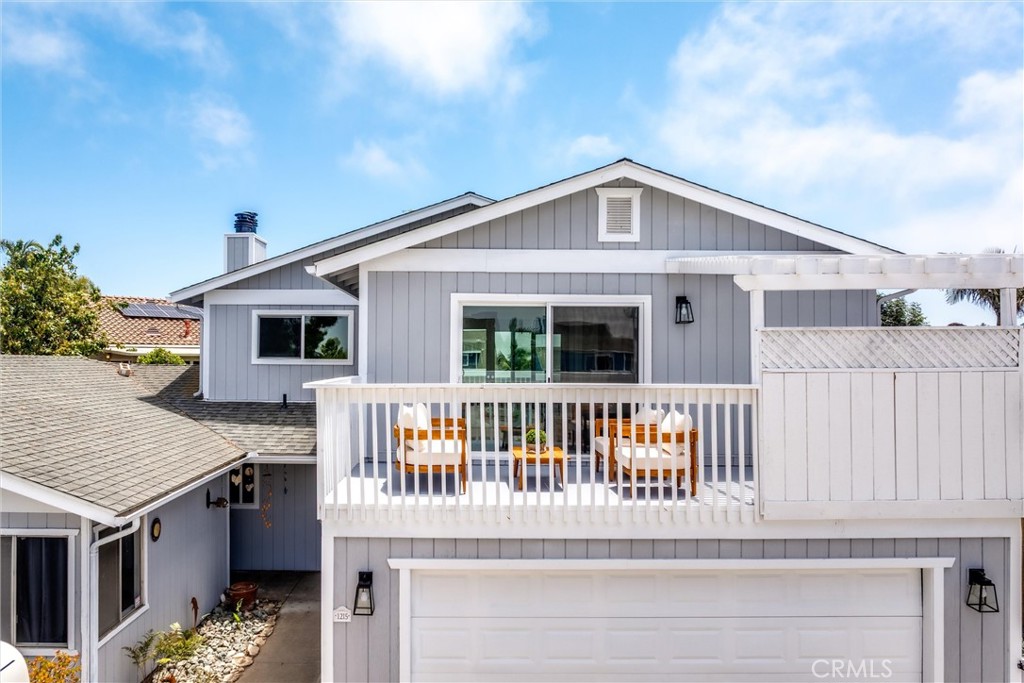 Gray two-story house with a white-railed deck, outdoor seating, and a wide garage.