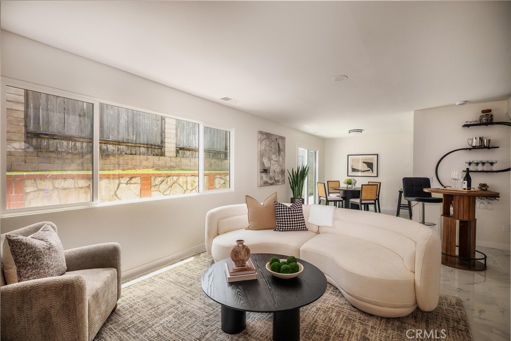 Furnished living room with a curved cream sectional and large windows overlooking a stone retaining wall.