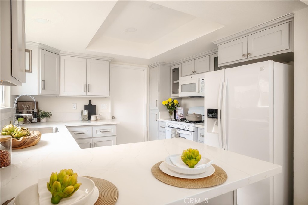 Bright white kitchen with a large marble-look island, paneled cabinetry, and white appliances.