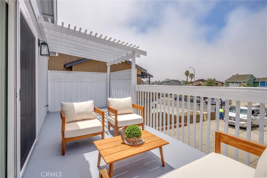 Covered patio with a white pergola, cushioned chairs, and a wooden coffee table overlooking the street.