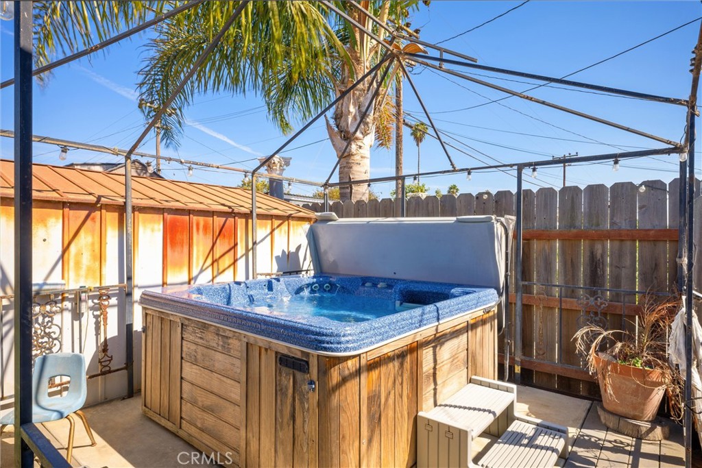 Outdoor hot tub on a fenced patio beneath a palm tree.