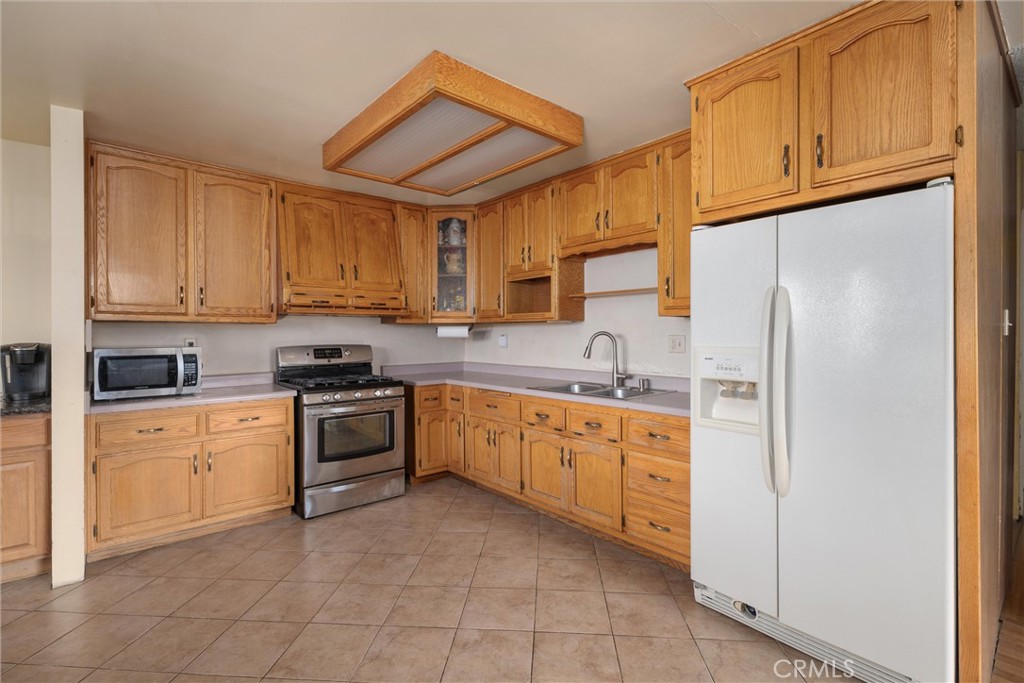 Kitchen with oak cabinets, tiled floor, stainless steel range, and white refrigerator.