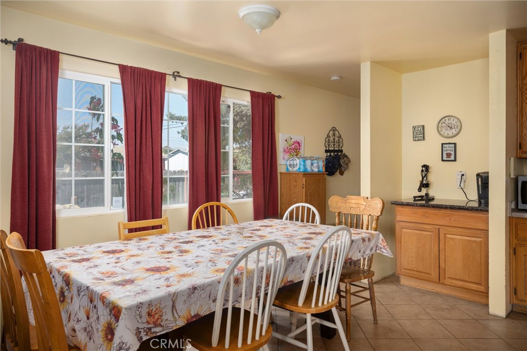 Dining area with a floral tablecloth, wooden chairs, red curtains, and large windows.