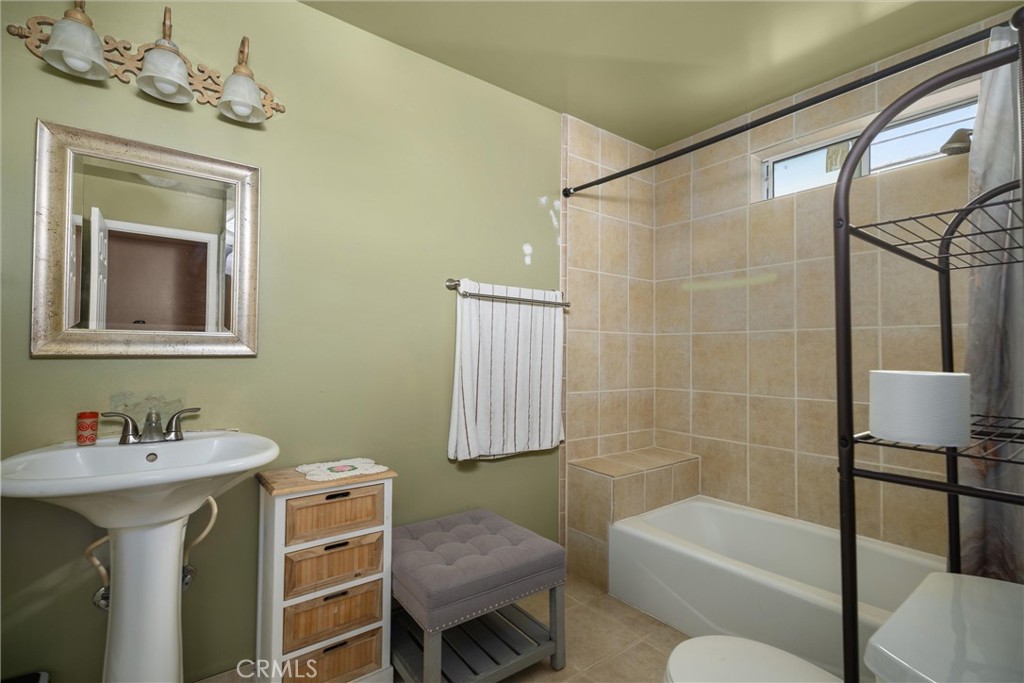Bathroom with a pedestal sink, tiled bathtub and shower, and high window.
