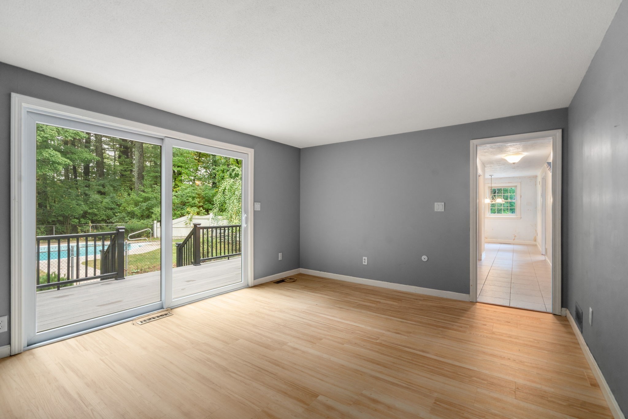 Empty gray-walled room with hardwood floors, sliding doors, and a view of the deck and pool.