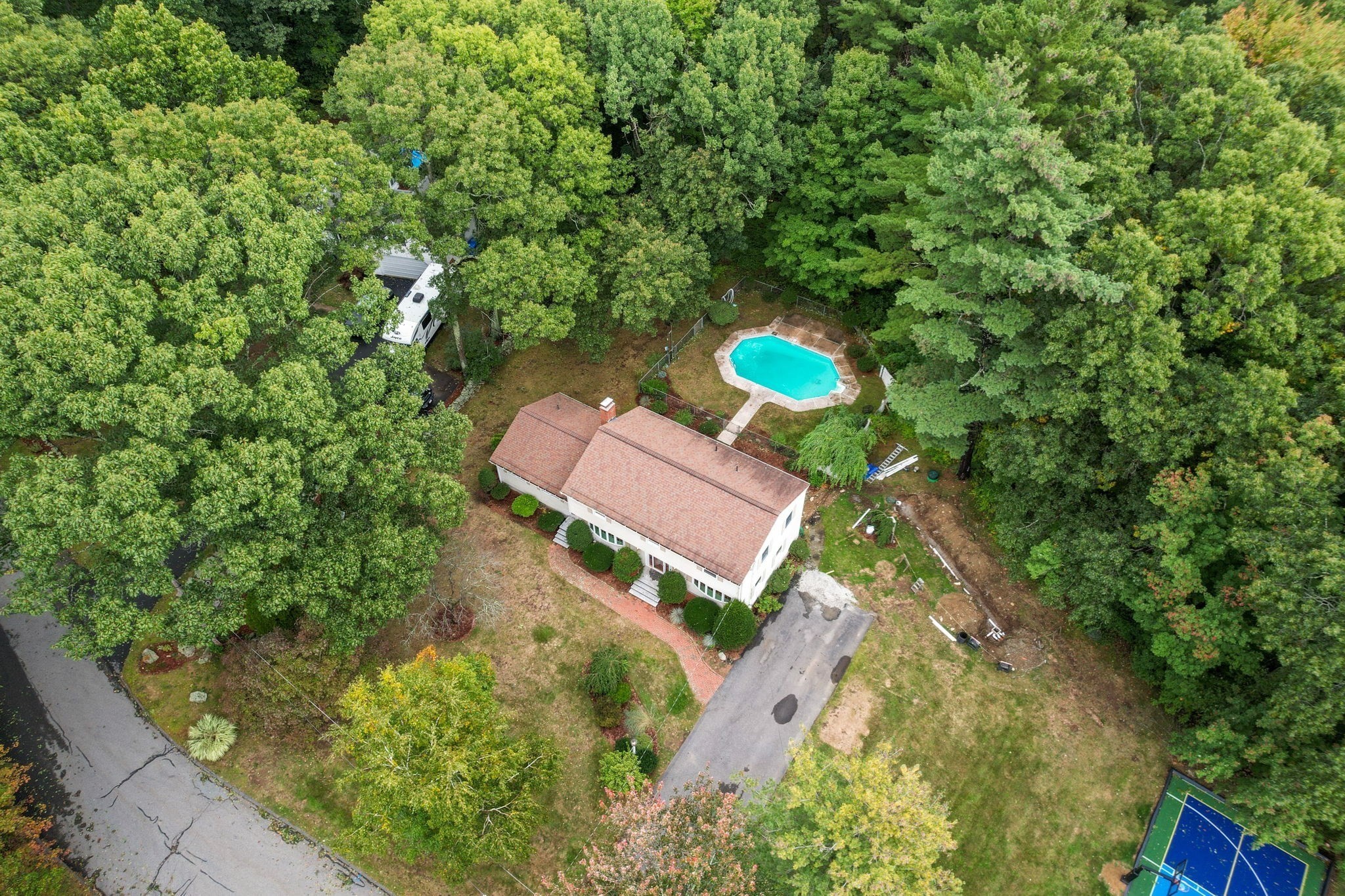 Aerial view of a wooded home with a backyard pool and sport court.
