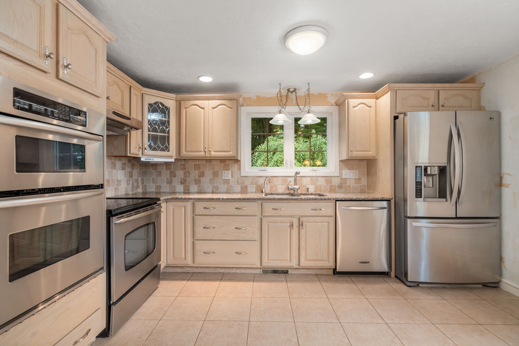 Kitchen with pale wood cabinetry, stainless steel appliances, and a window overlooking greenery.