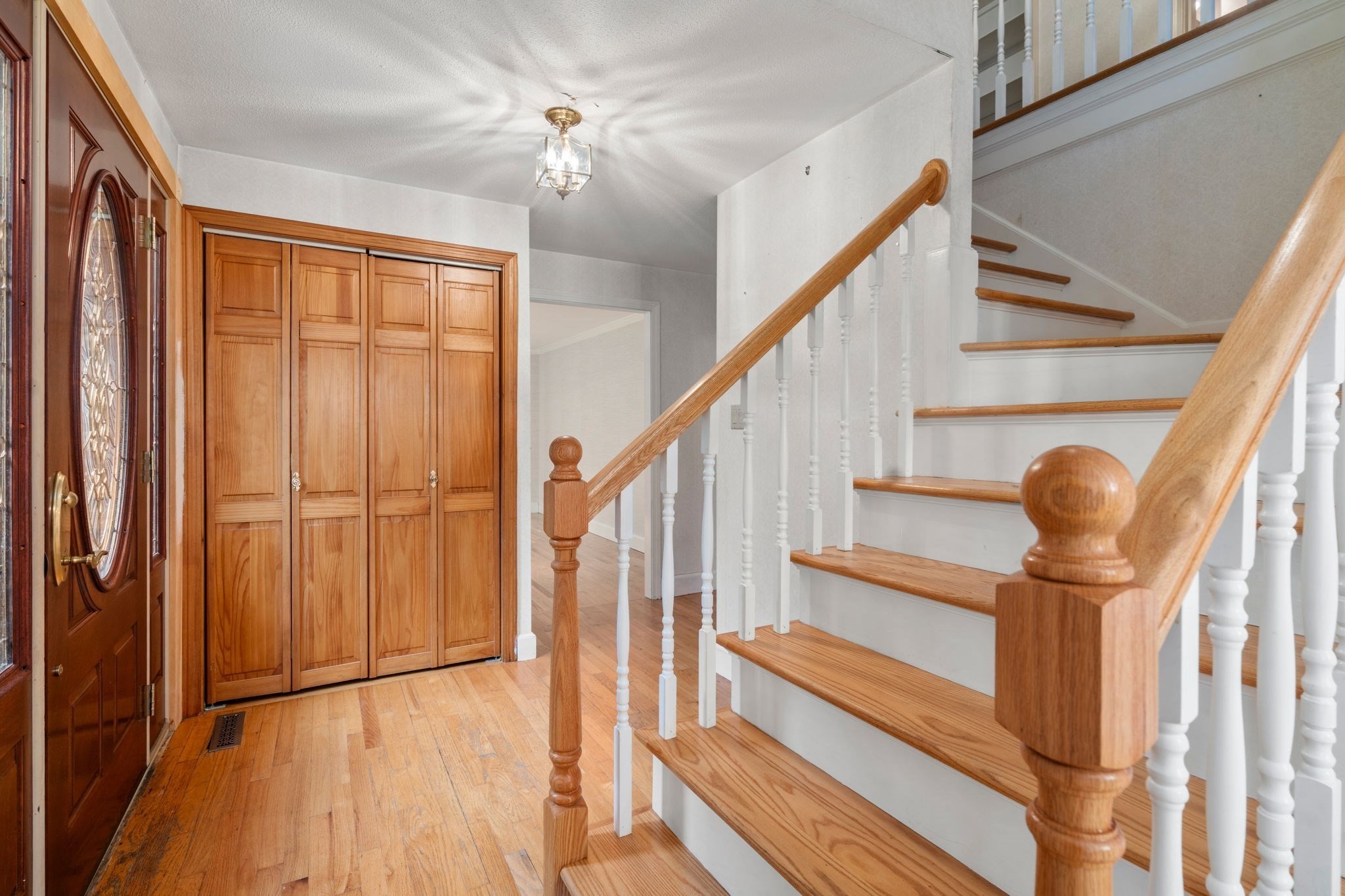 Entry foyer with built-in wood closets and a staircase with wood treads and white balusters.