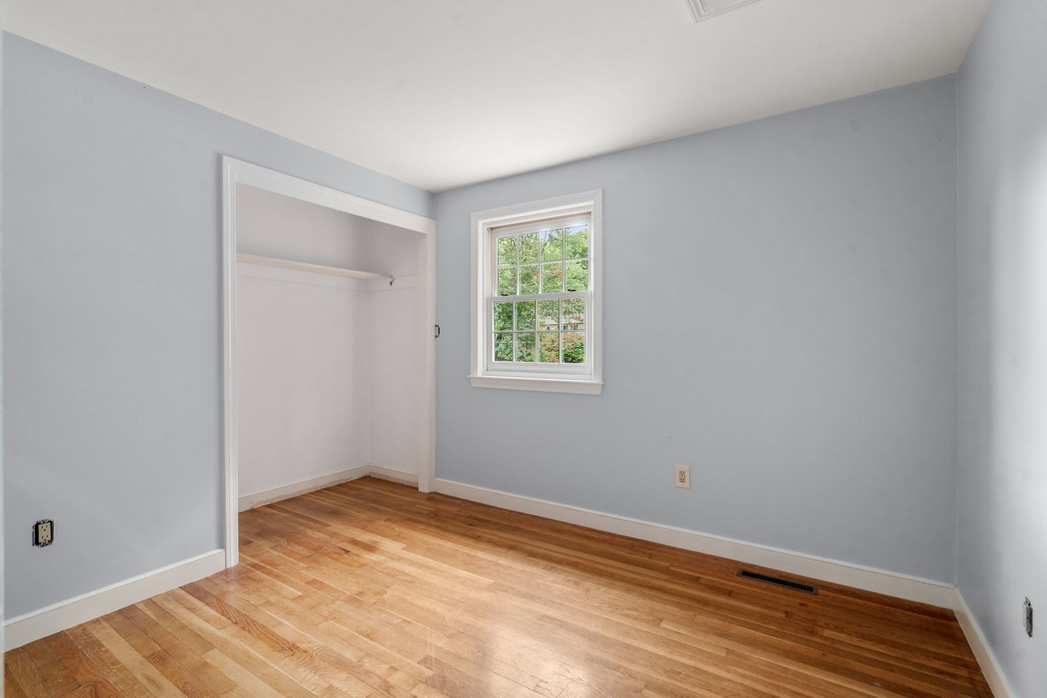 Empty bedroom with hardwood floors, a white-trimmed window, and an open closet alcove.