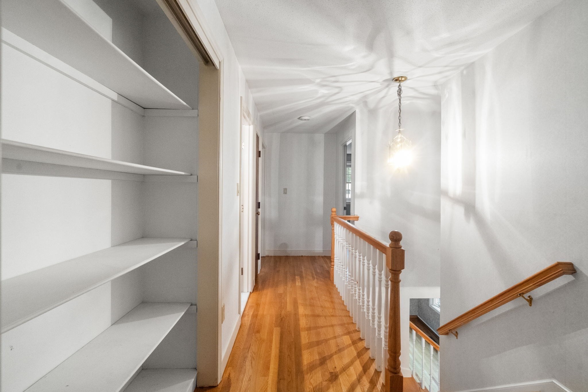Upstairs hallway with built-in white shelves, hardwood floors, and a wood-and-white stair railing.
