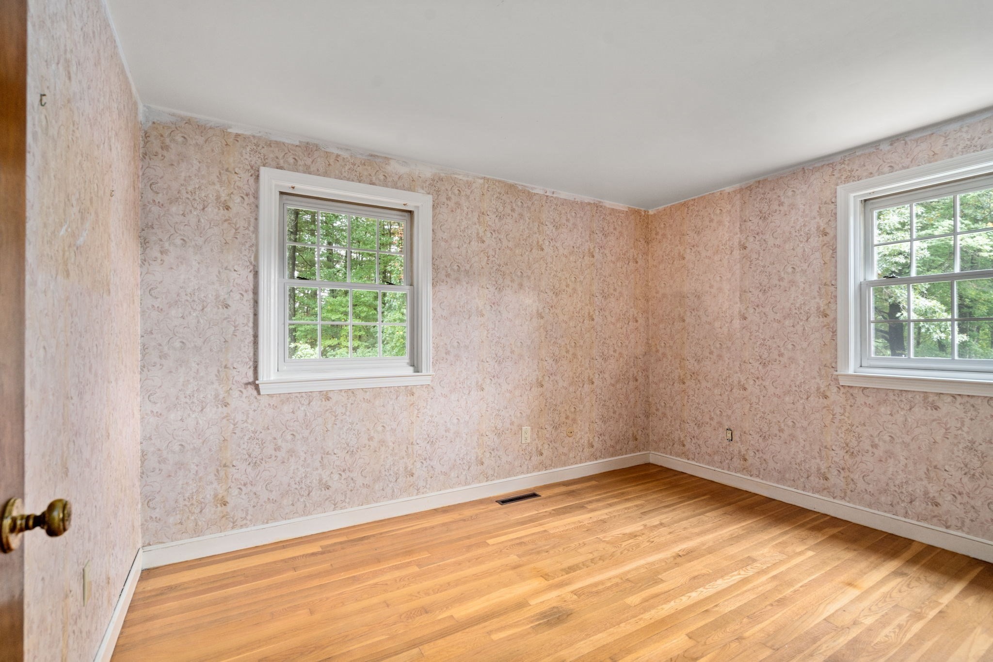 Empty bedroom with floral wallpaper, two windows, and hardwood floors.