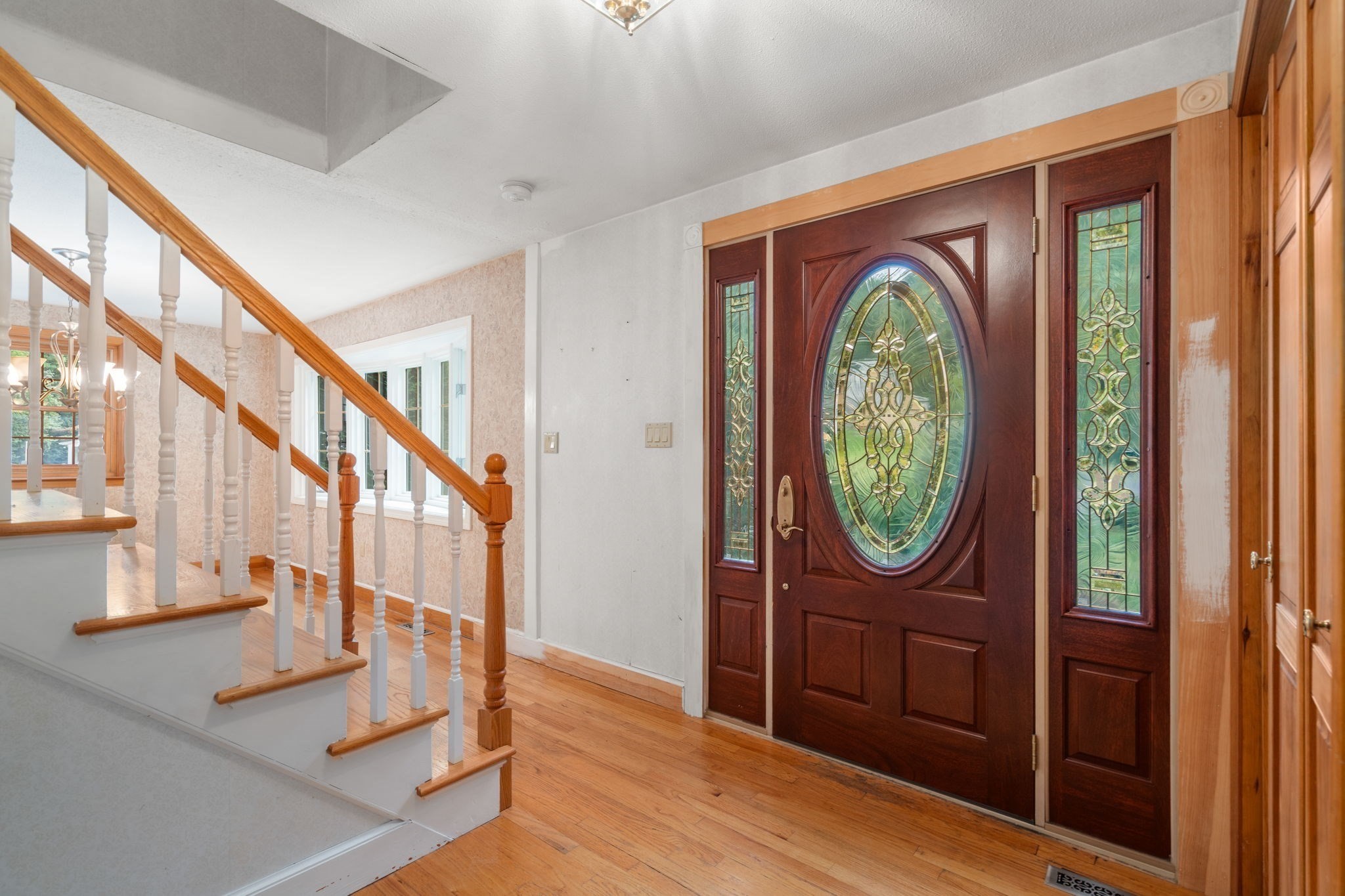 Foyer with an oval stained-glass front door, wood-railed staircase, and hardwood floors