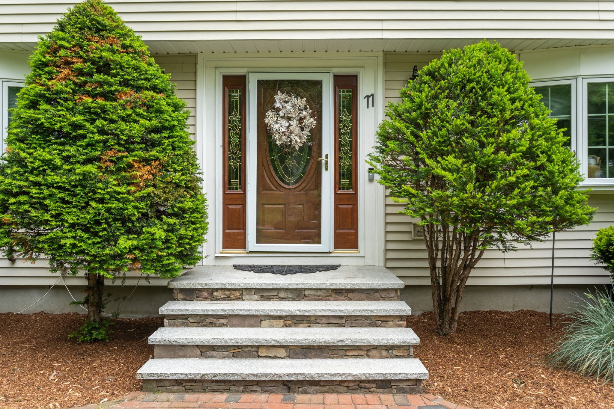 Front entrance with a decorative glass door, stone steps, and evergreen shrubs.