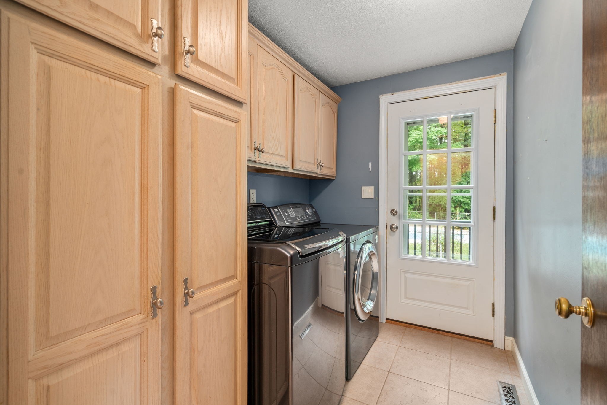 Laundry room with wood cabinets, washer and dryer, and a glass-paneled door.
