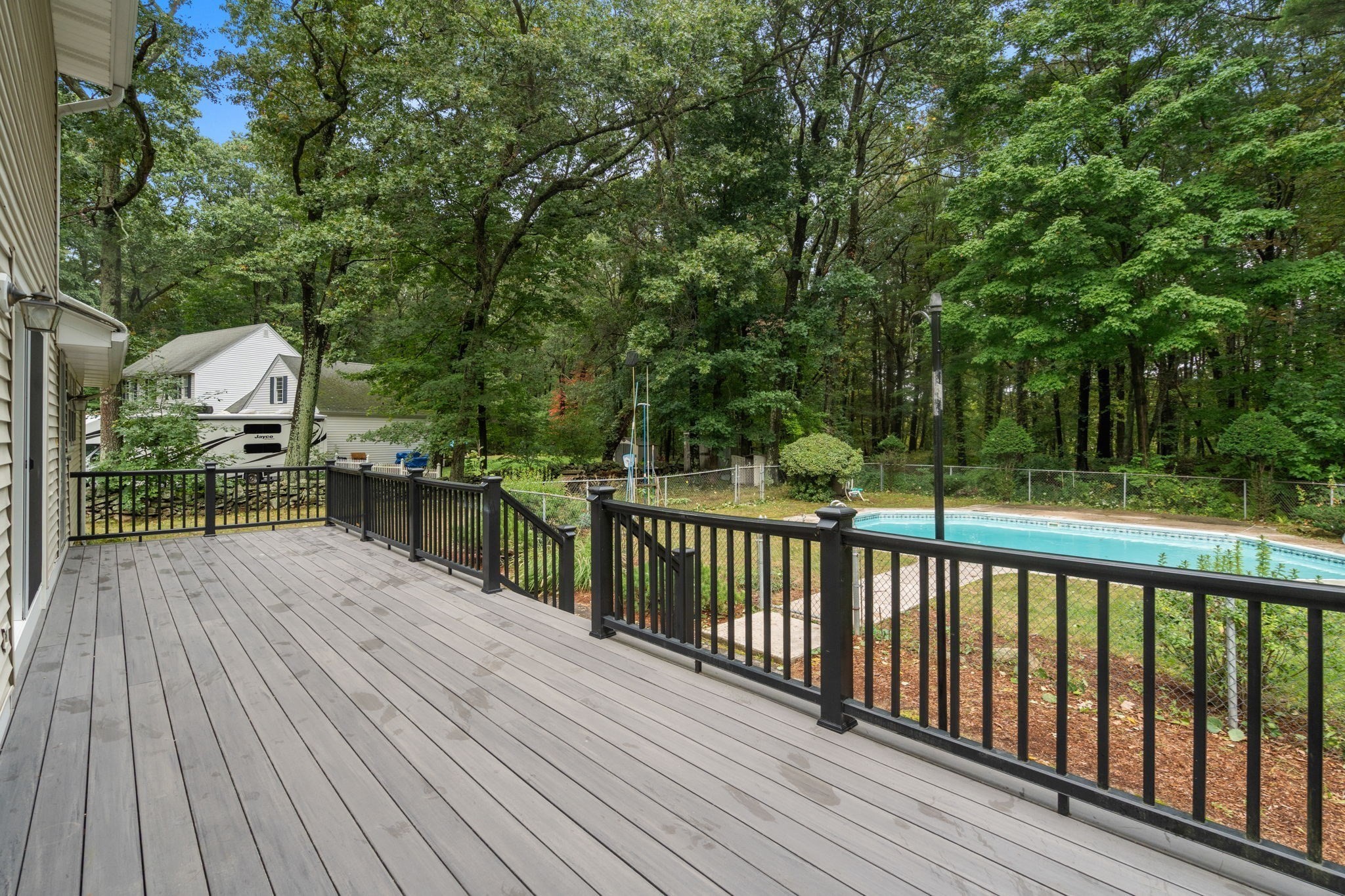 Gray deck with black railings overlooking a swimming pool and wooded backyard.