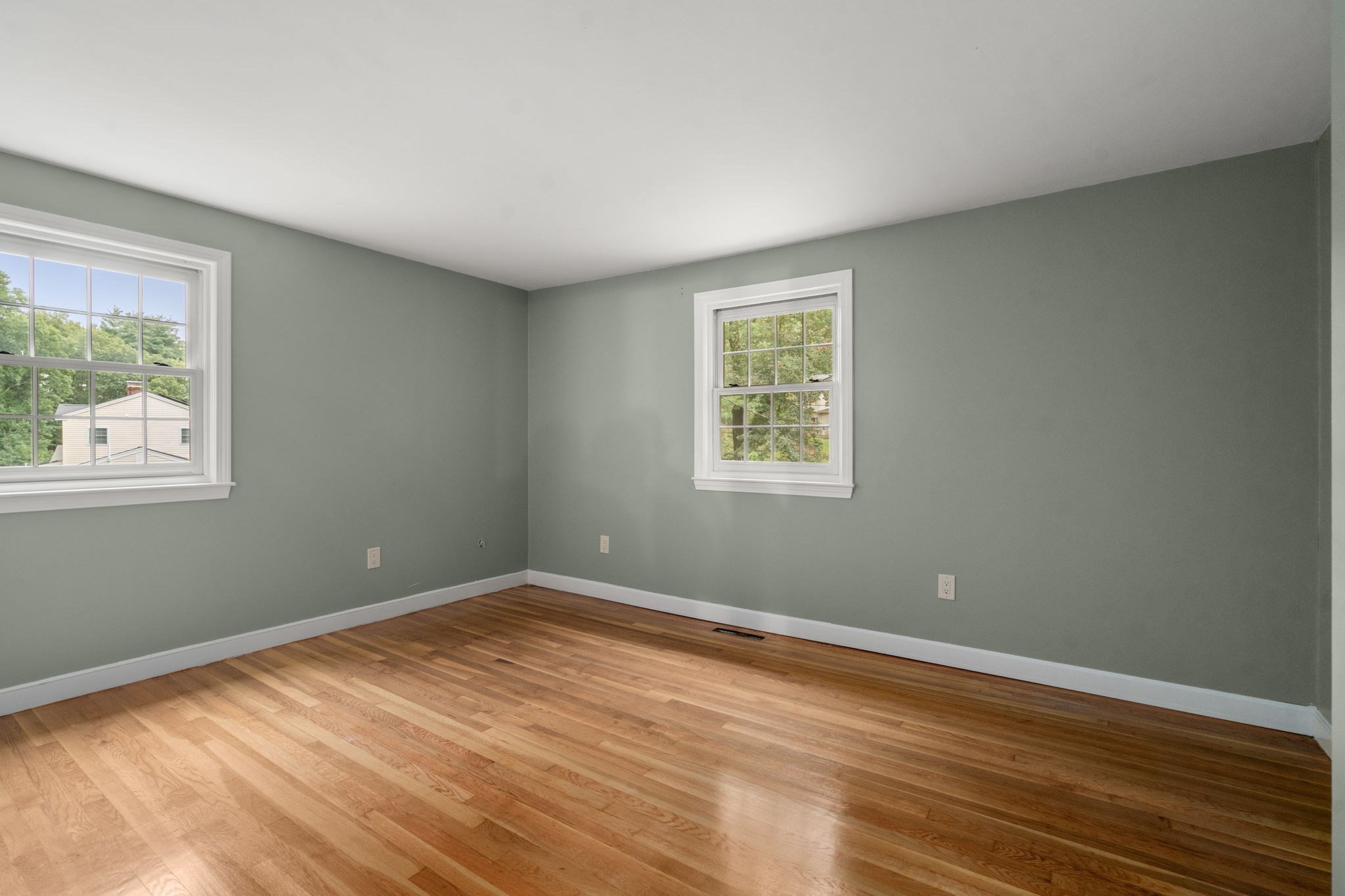 Empty room with green-gray walls, two windows, and polished hardwood floors.