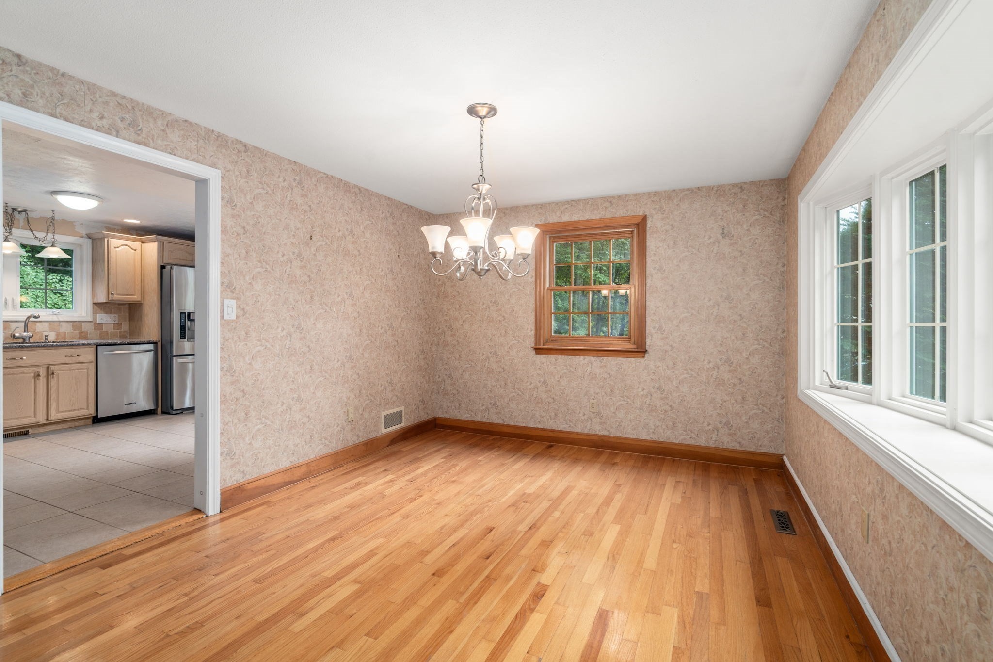 Empty dining room with hardwood floors, a chandelier, and an adjoining kitchen.