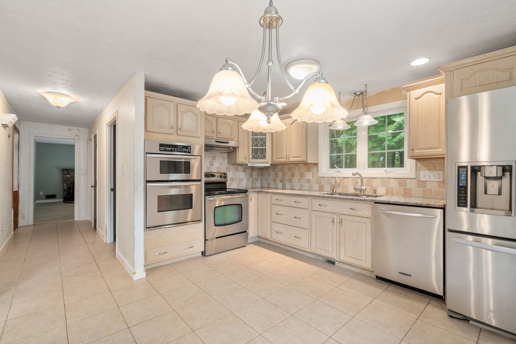 Kitchen with light wood cabinets, stainless steel appliances, and a window overlooking trees.