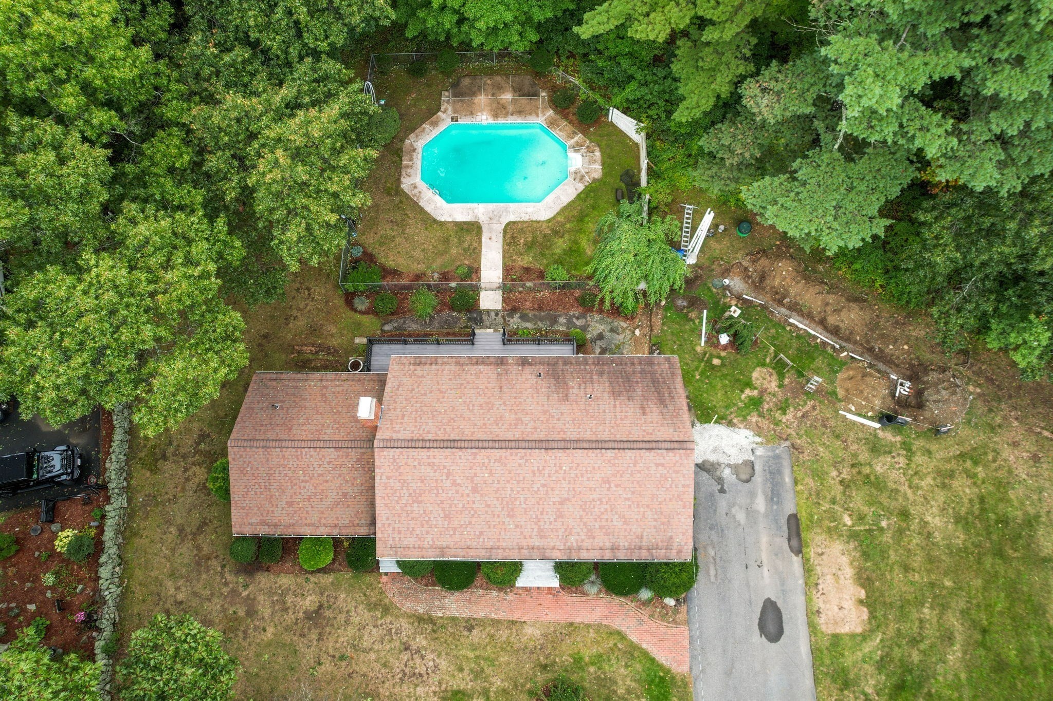 Aerial view of a house and wooded yard with an octagonal swimming pool behind it.