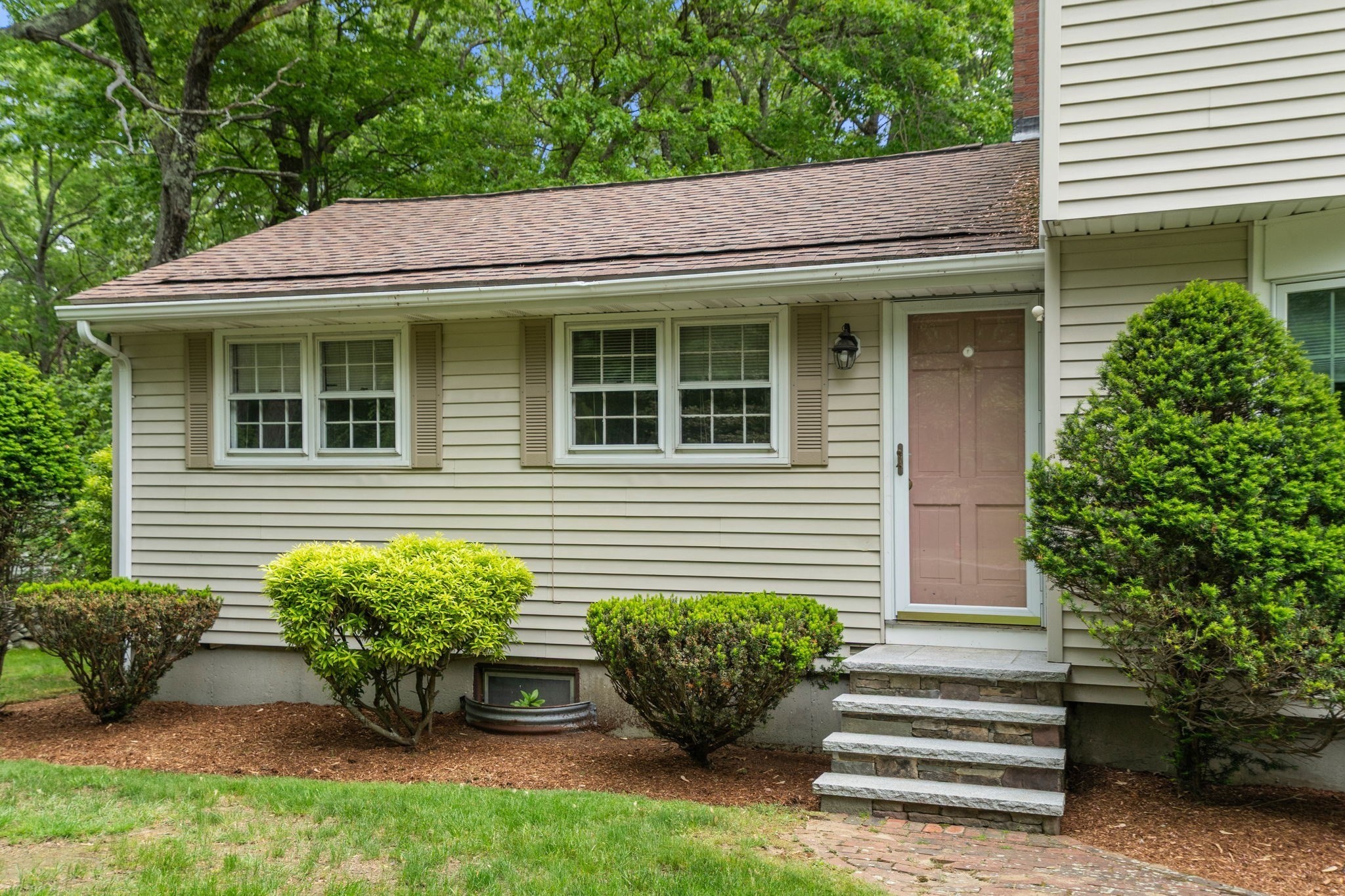 Home entrance with beige siding, brown door, stone steps, and landscaped shrubs.