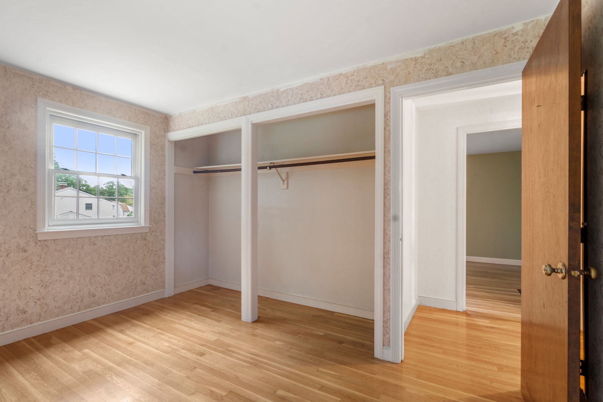 Empty bedroom with floral wallpaper, hardwood floors, and a large open closet.