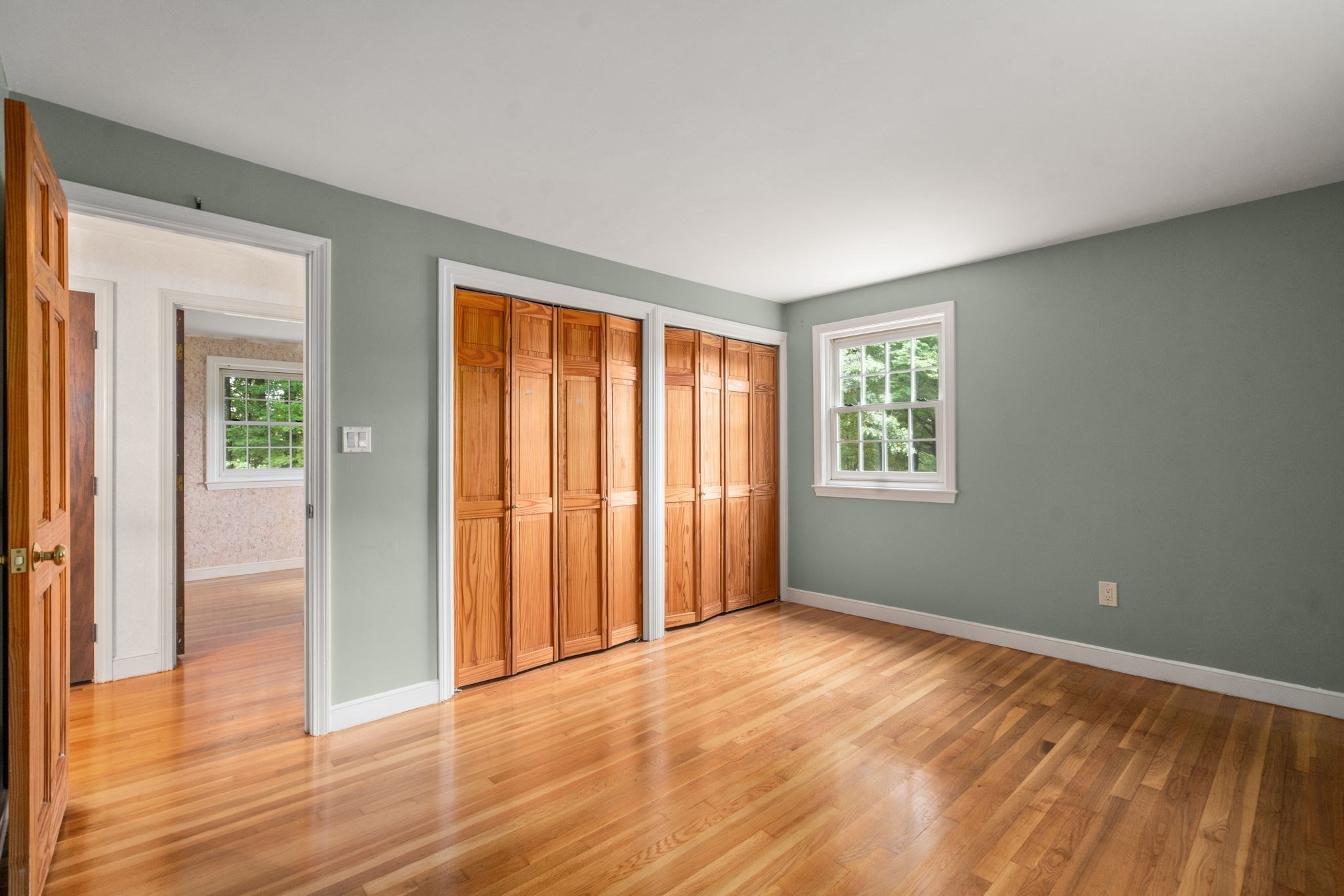 Empty bedroom with hardwood floors, wooden folding closet doors, and a window.