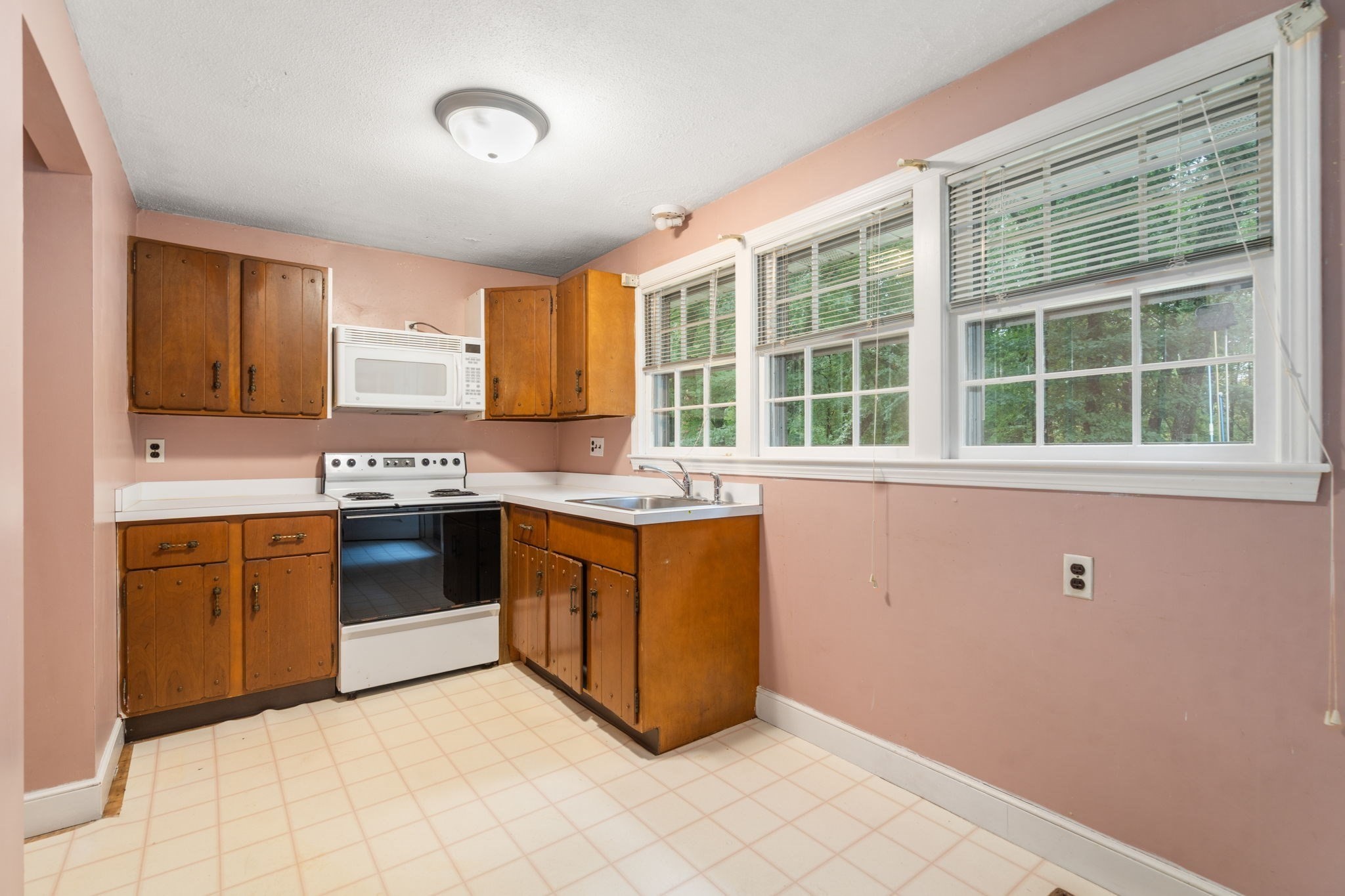 Kitchen with honey-brown wood cabinets, pink walls, and large windows above the sink.
