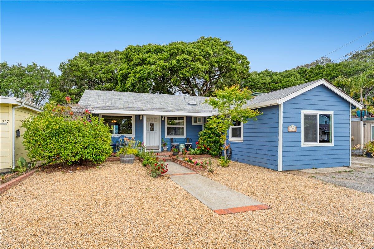 Blue single-story home with white trim, a gravel yard, and a flower-lined walkway.