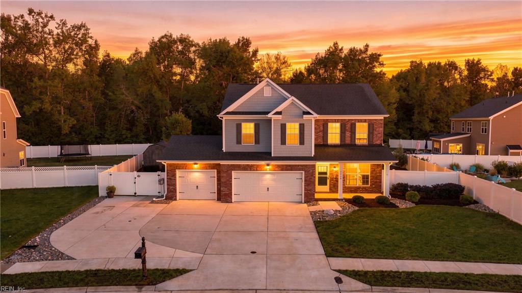 Two-story brick and gray house with a wide driveway and fenced yard at sunset.