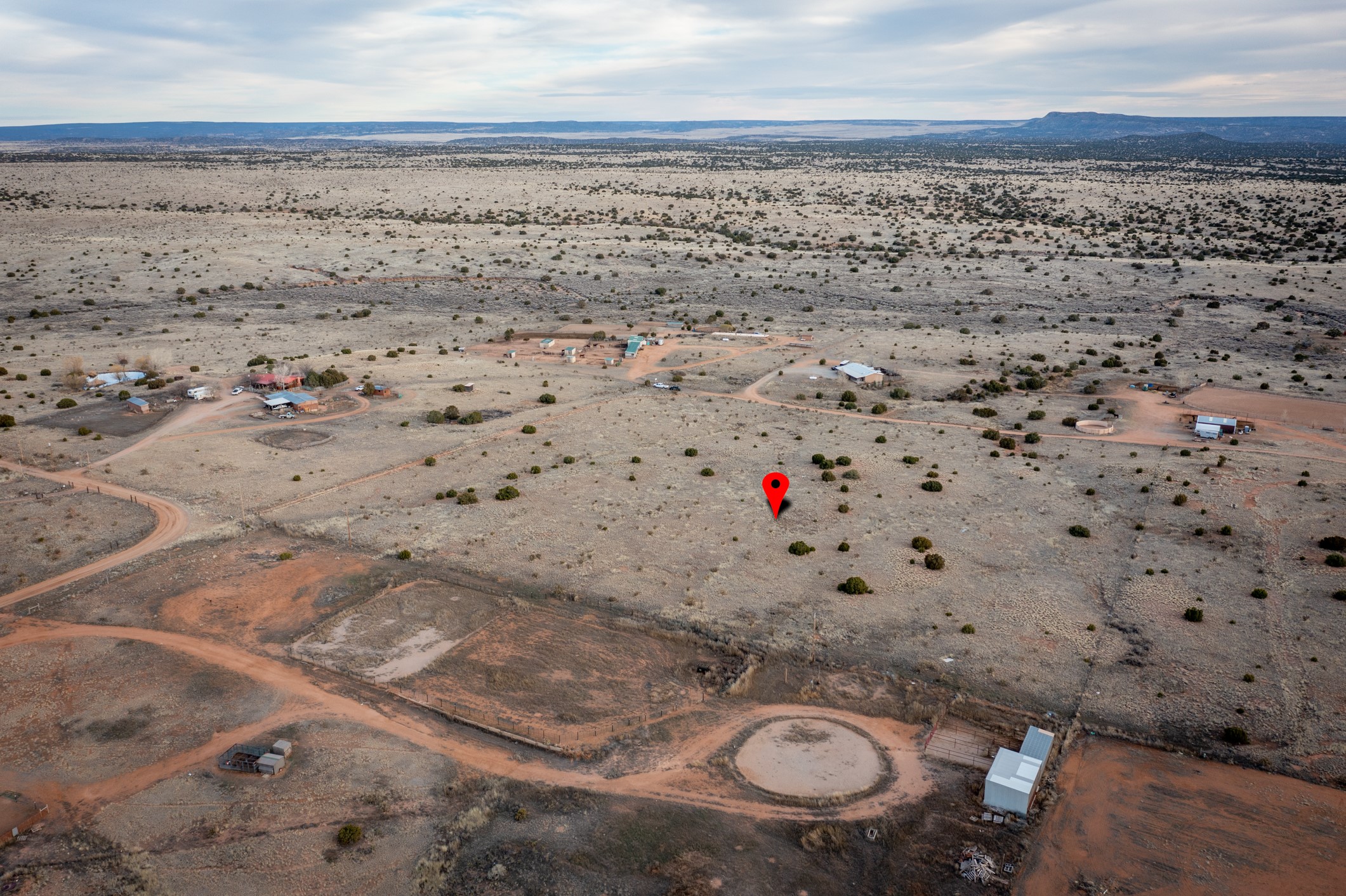Aerial view of dry rural land marked by a red pin, with dirt roads and distant mesas.