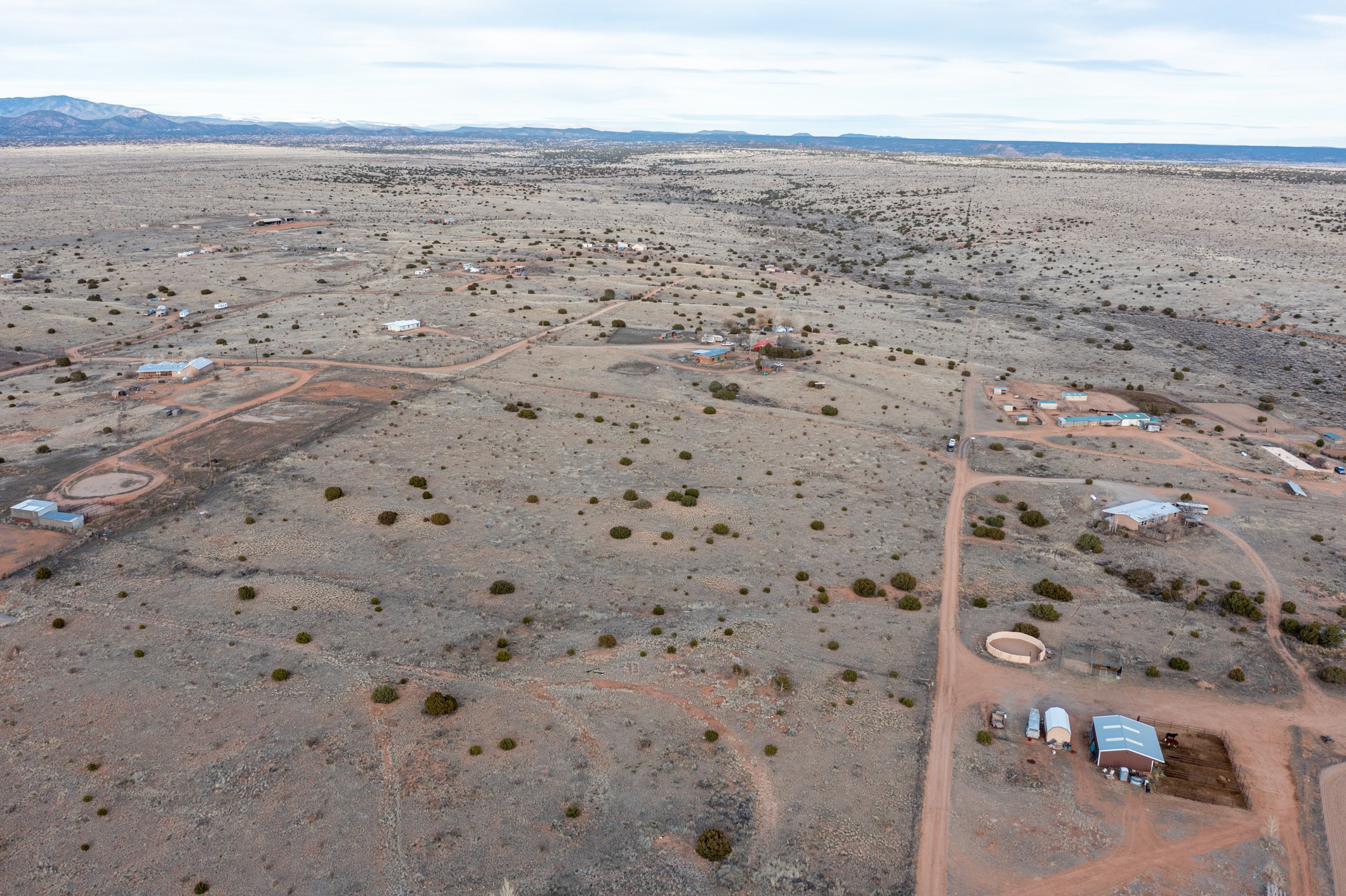 Aerial view of arid rural land with dirt roads, scattered buildings, and distant mountains.