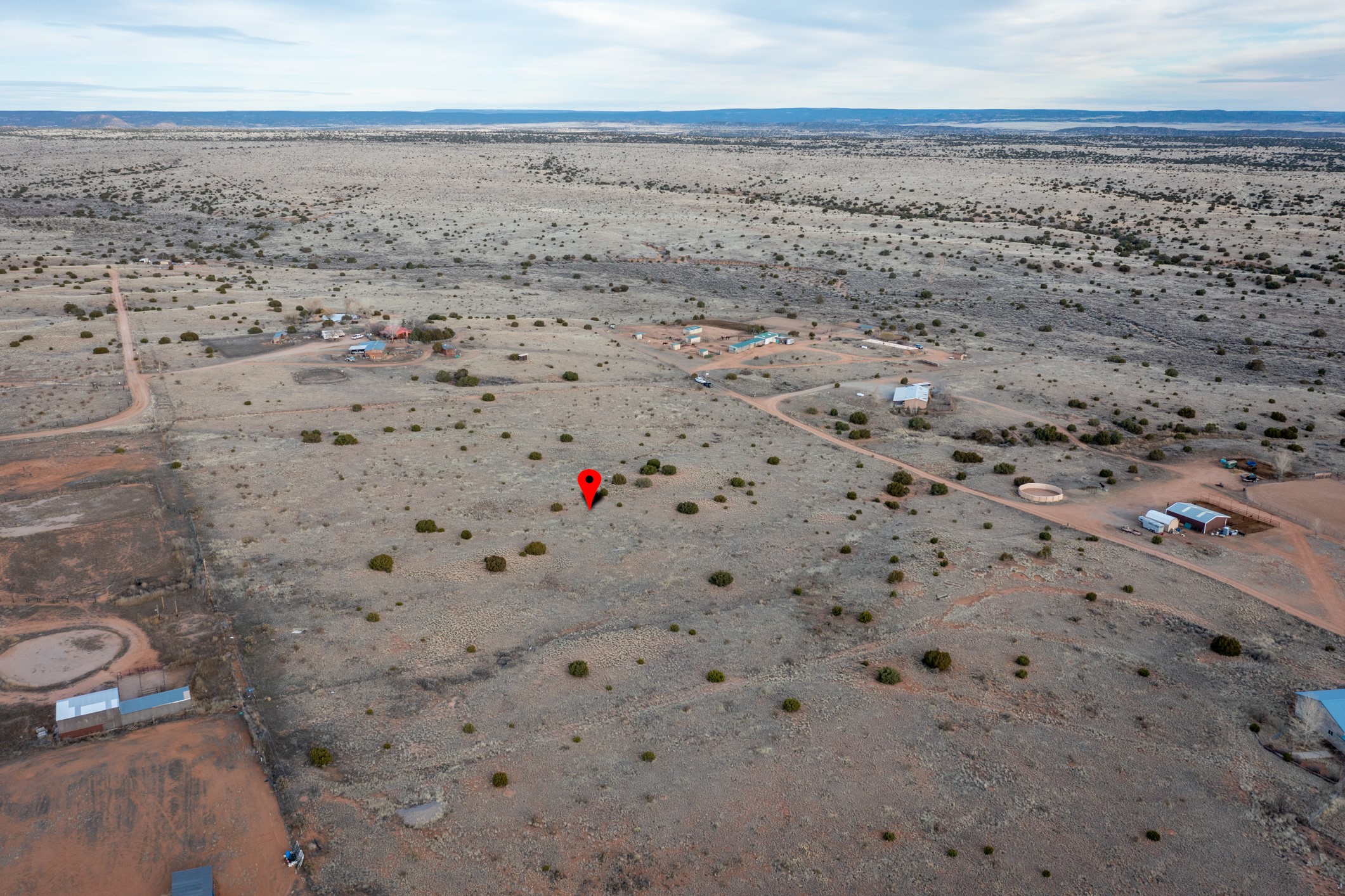 Aerial view of scrubland marked with a red pin, with dirt roads and scattered buildings nearby.
