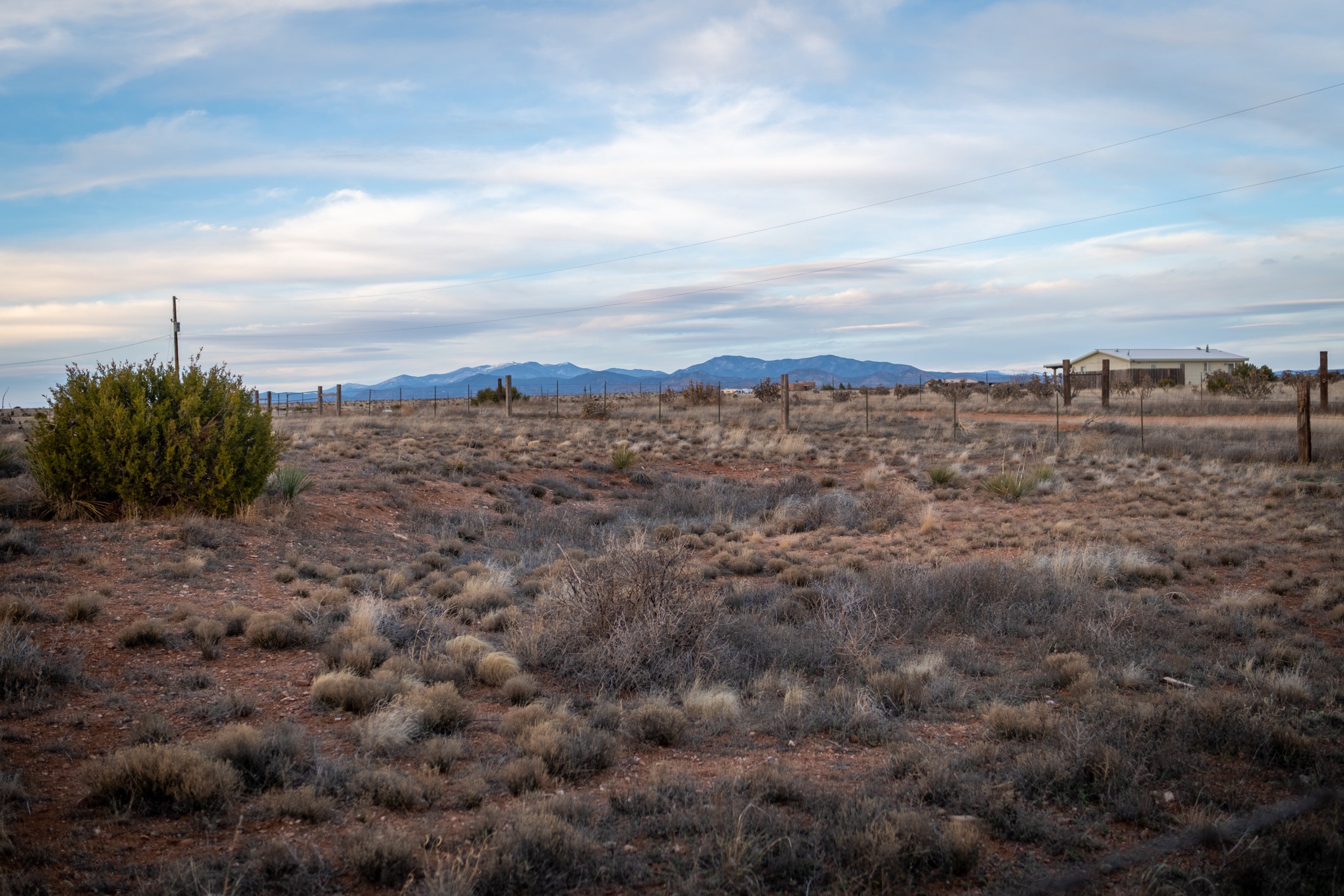 Vacant scrubland lot with reddish soil, a fenced boundary, and distant mountains.