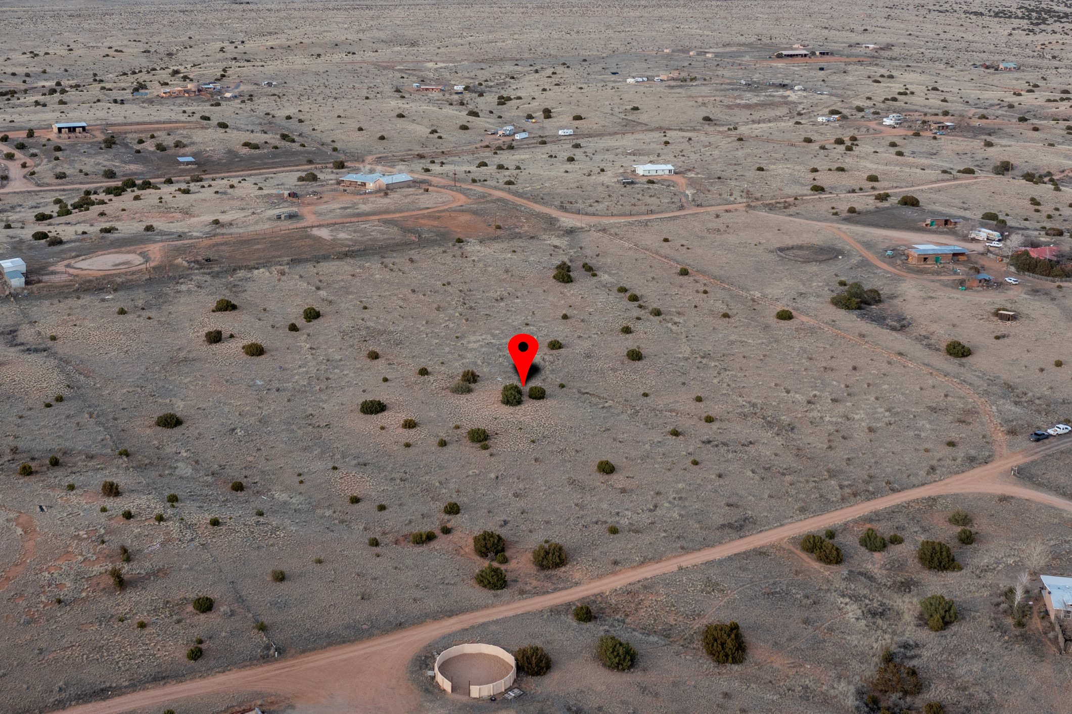 Aerial view of a scrub-covered rural lot marked by a red location pin, with dirt roads nearby.