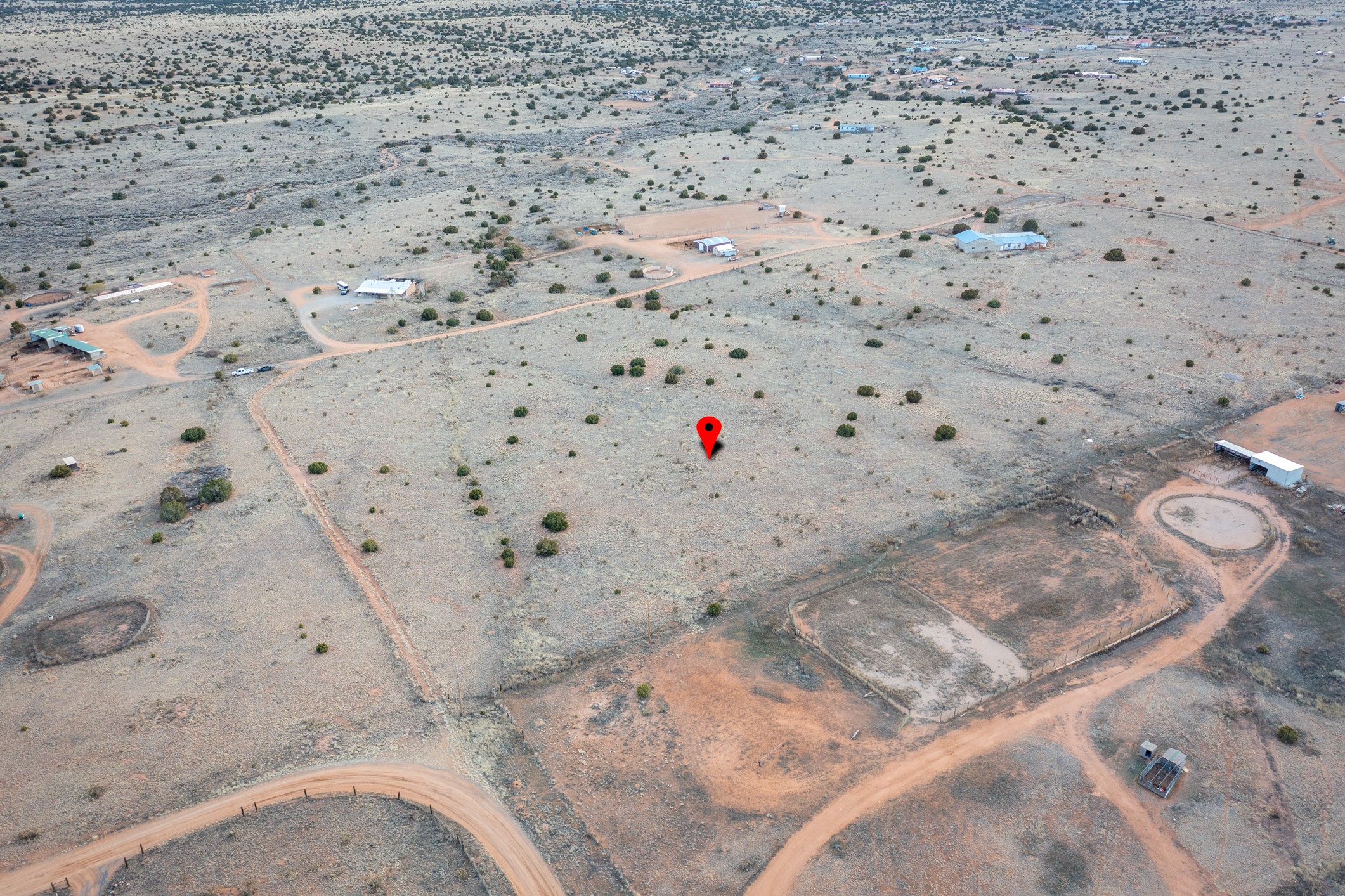 Aerial view of vacant high-desert land marked by a red pin, with dirt roads and scattered rural buildings.