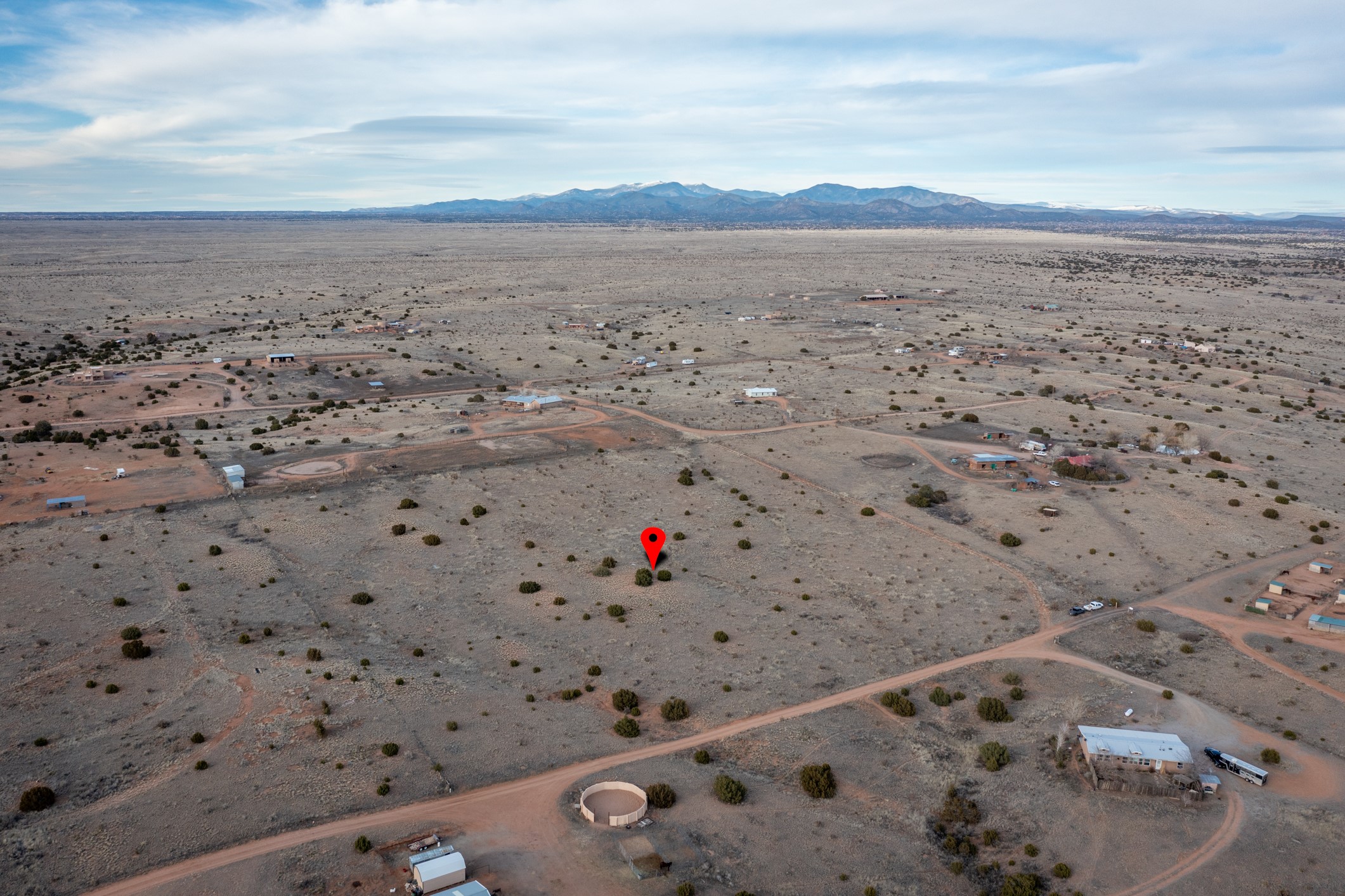 Vacant high-desert parcel marked by a red pin, with scattered homes and mountains beyond.