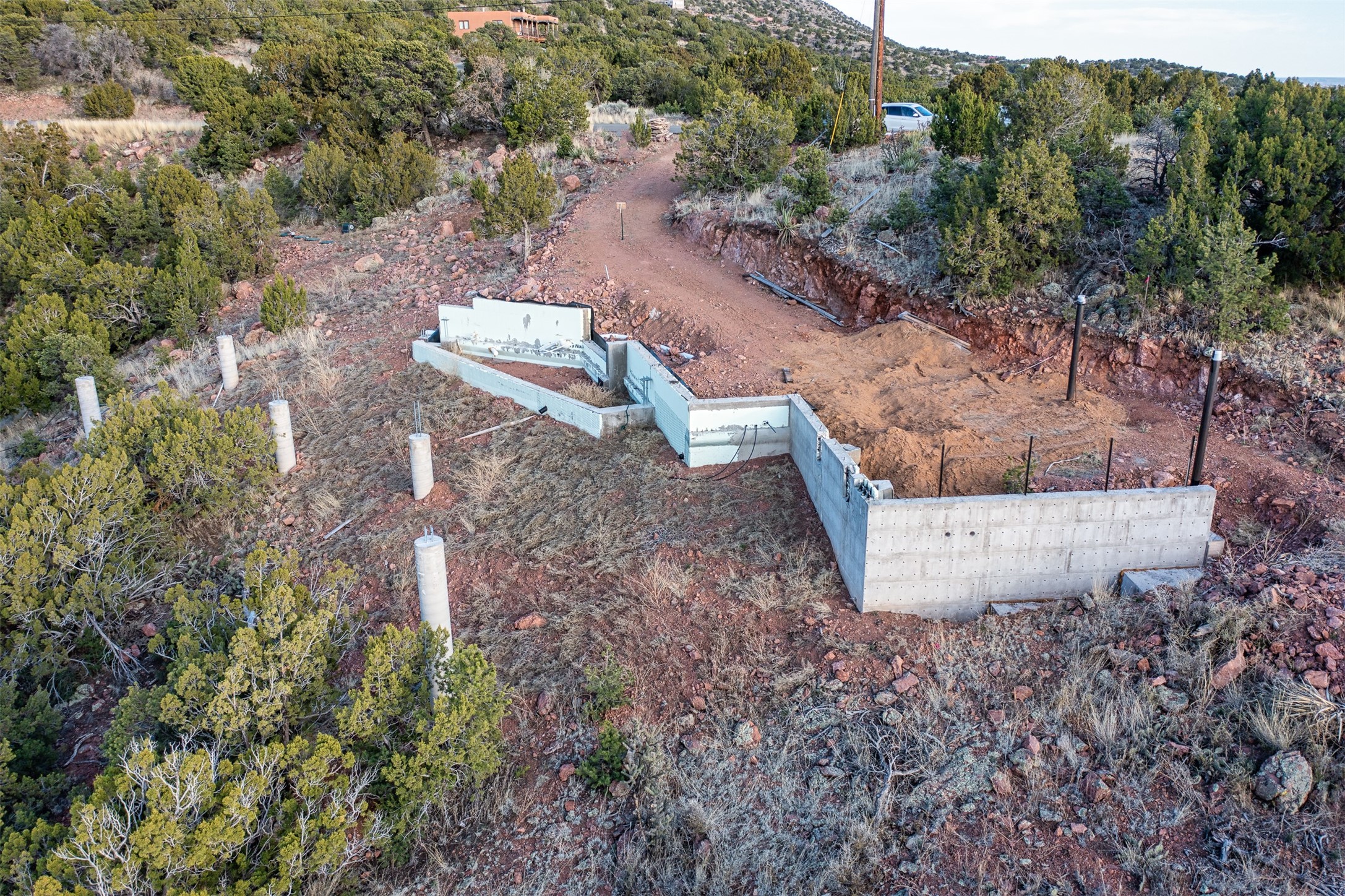 Partially built concrete foundation on a rocky, sloping lot with a dirt access drive.