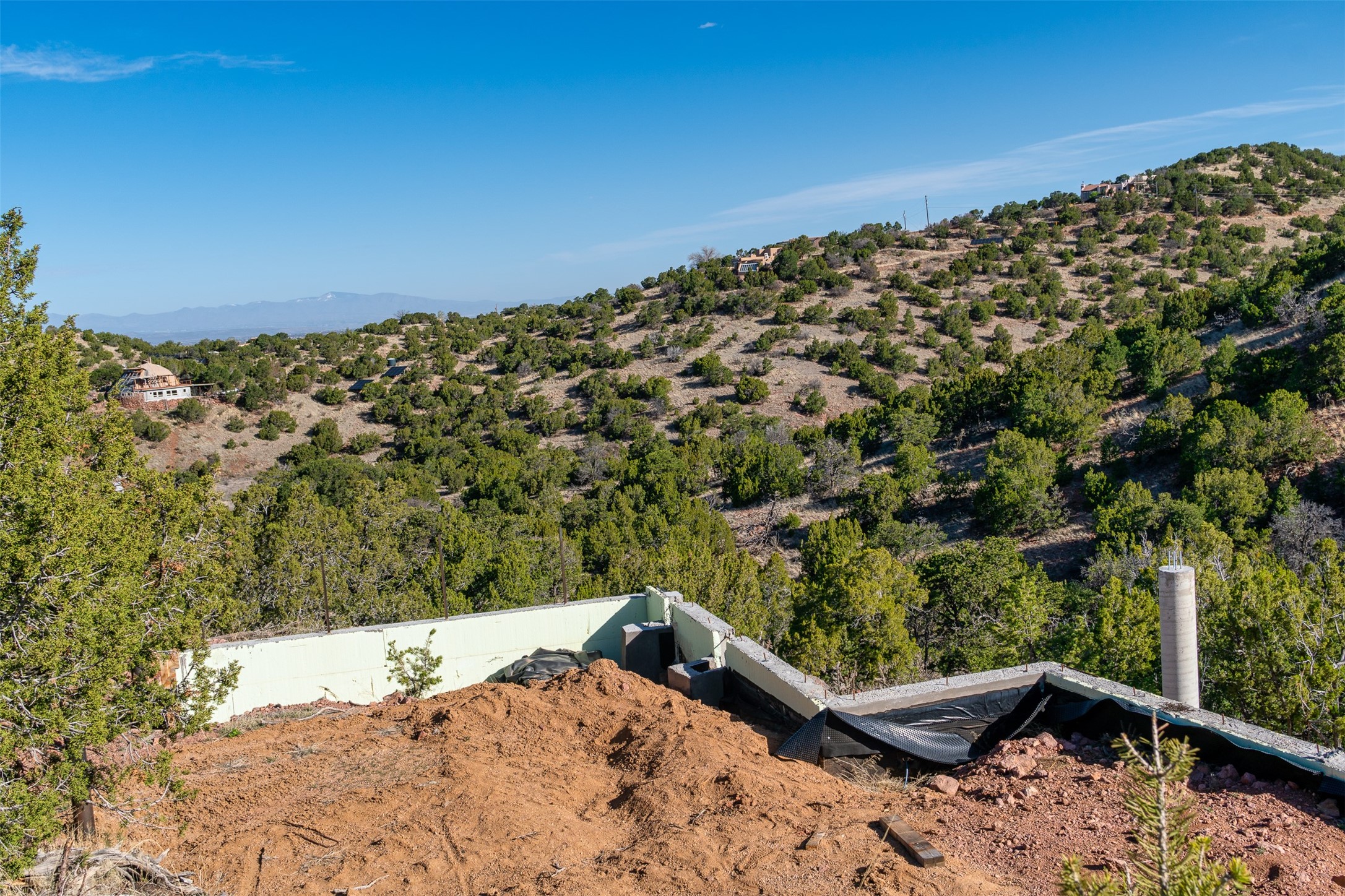 House foundation under construction on a wooded hillside, with distant mountain views.