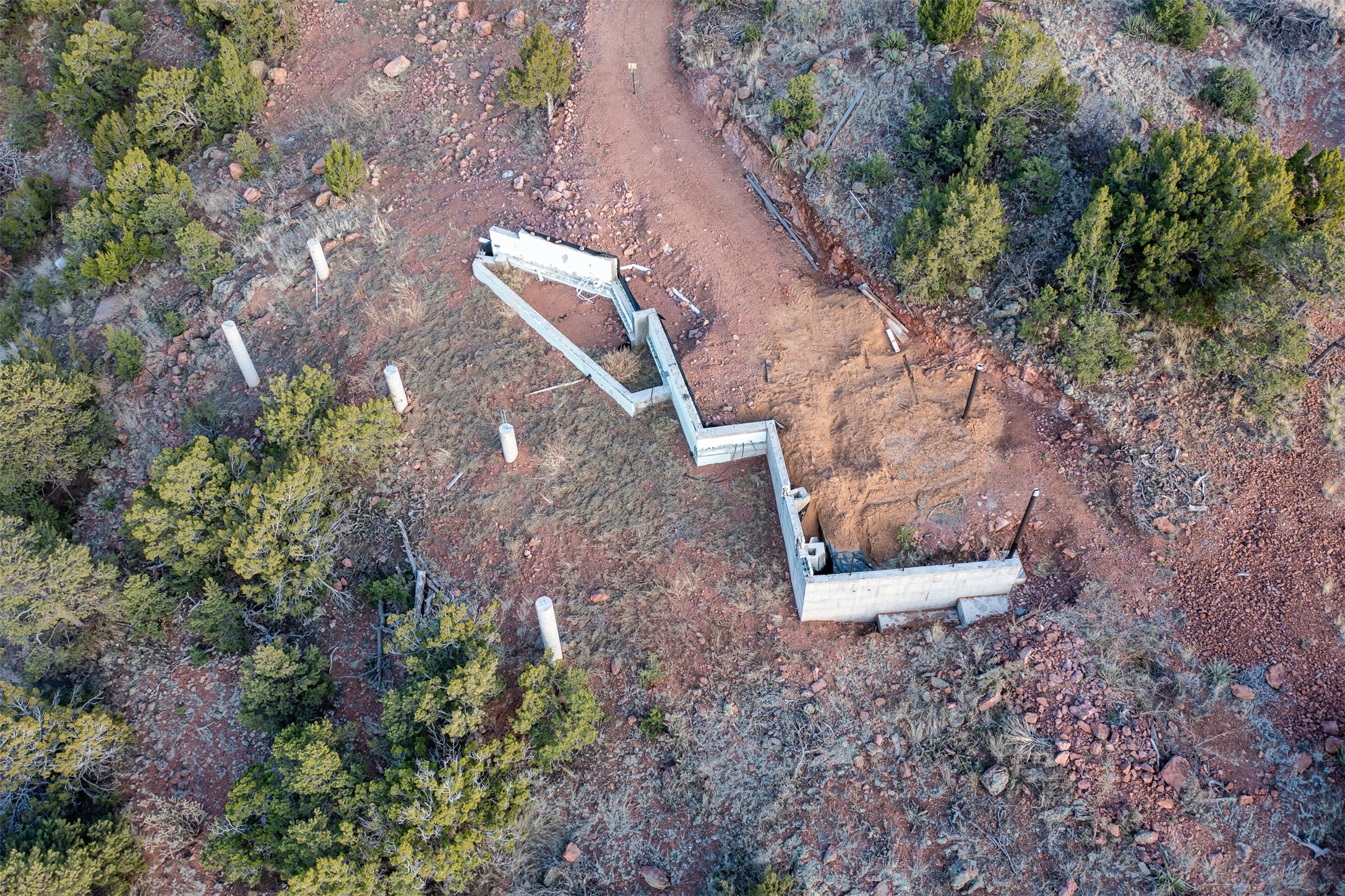 Aerial view of a concrete foundation under construction amid rocky scrubland and evergreen trees.