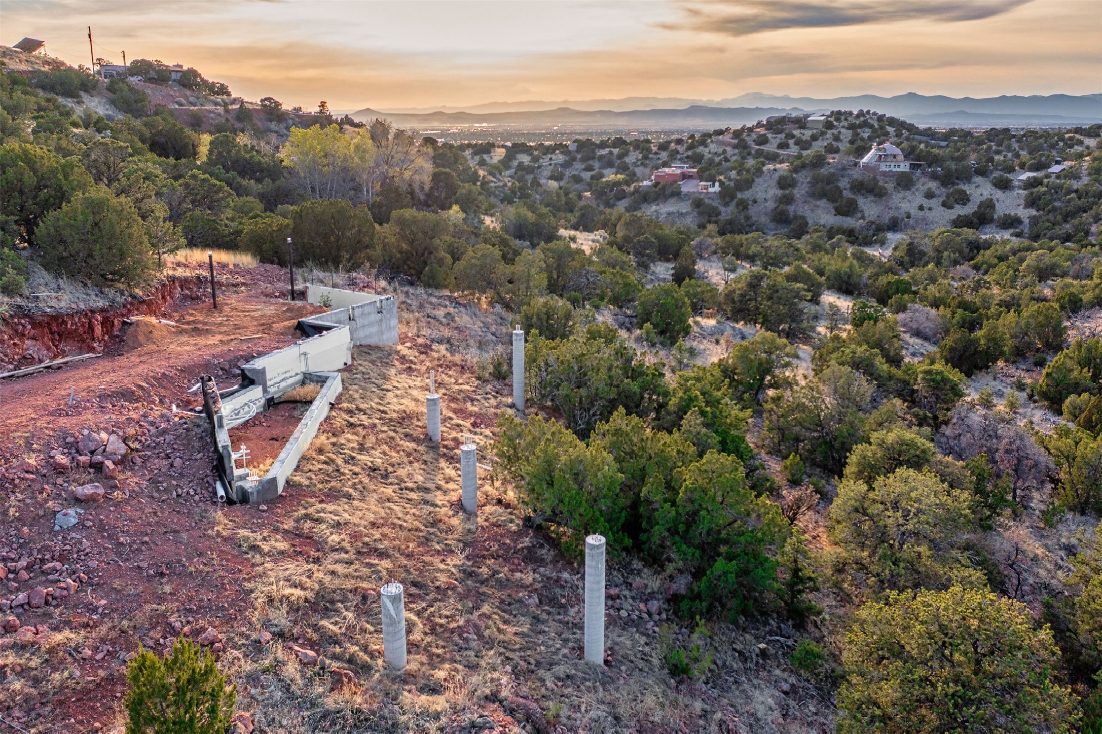 Hillside construction site with concrete foundation piers overlooking a wooded valley and distant mountains.