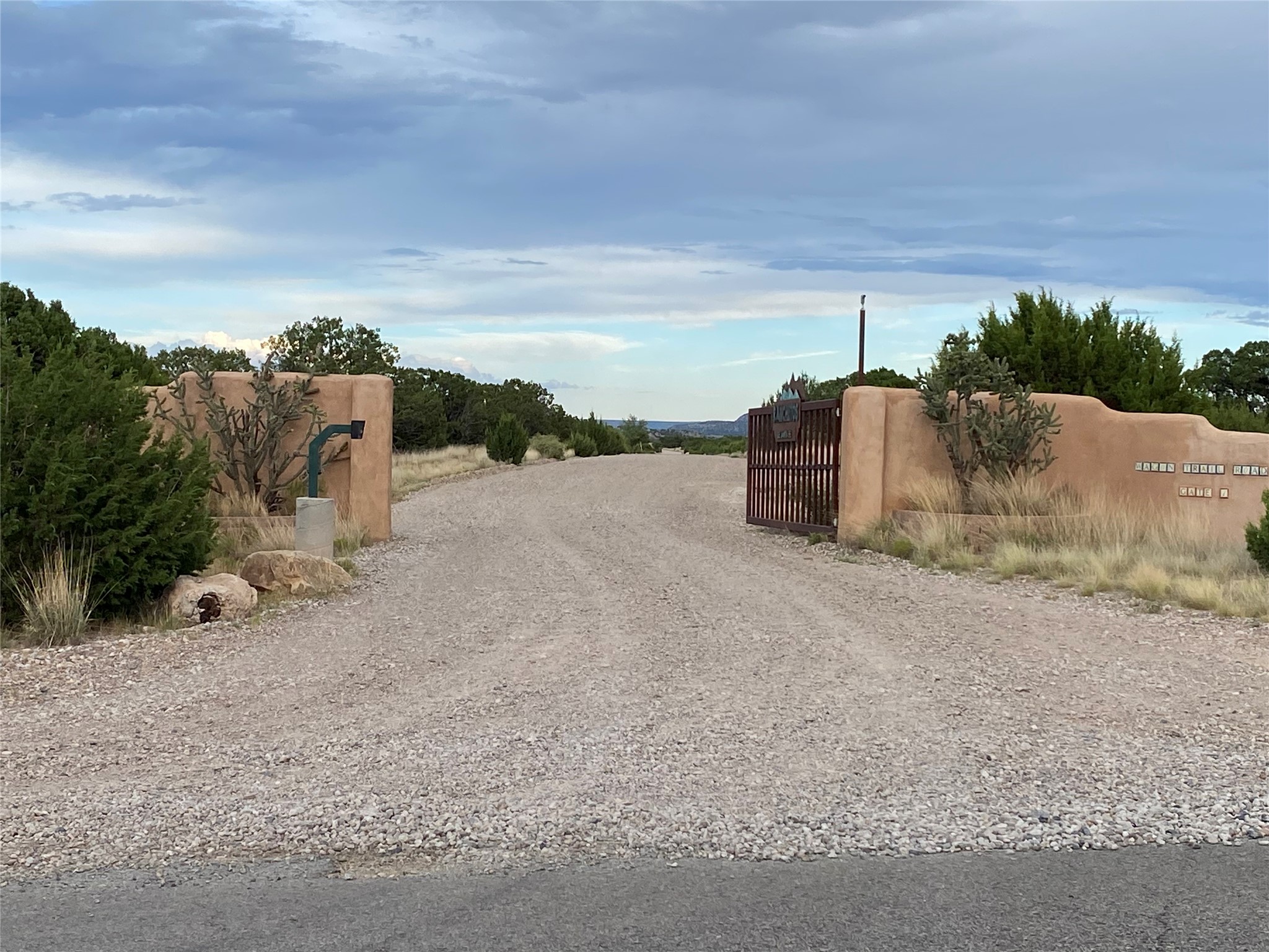 Gravel driveway entrance with an open metal gate between tan stucco walls marked 176 Wagon Trail Road.