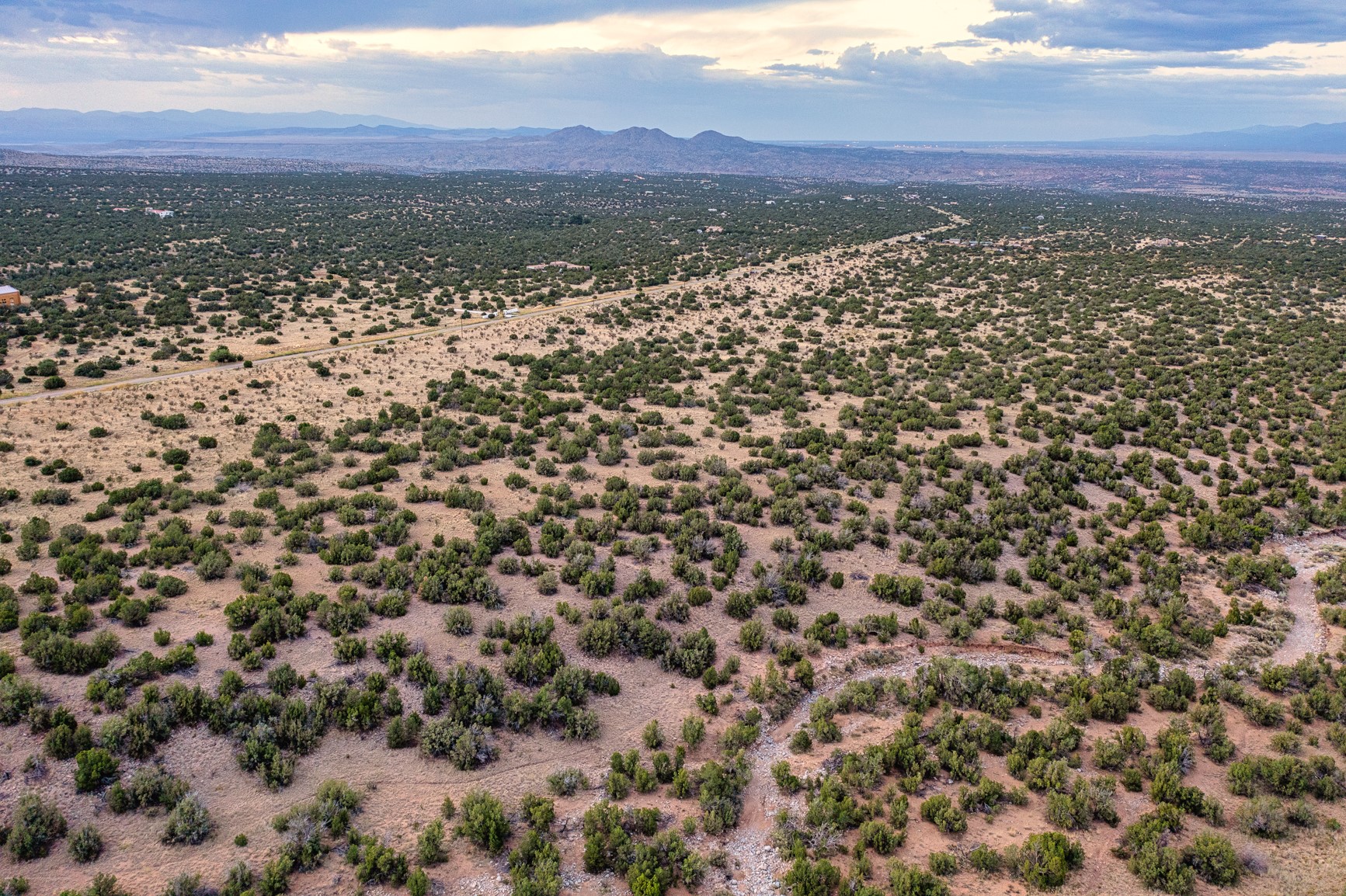 Aerial view of scrub-covered vacant land, with a road crossing it and mountains in the distance.
