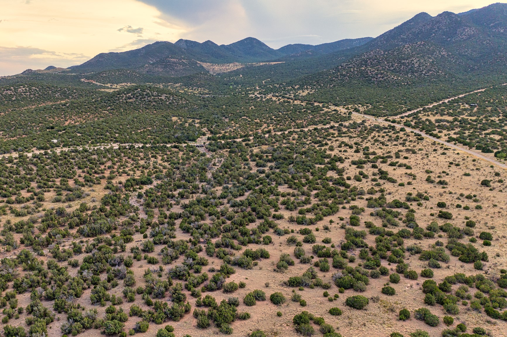 Aerial view of scrub-covered land with a winding road and mountain range beyond.