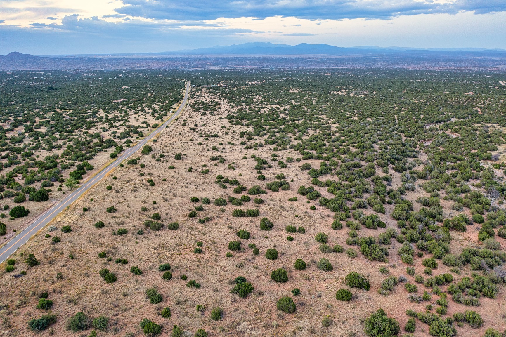 Aerial view of scrub-covered vacant land beside a road, with distant development and mountains.