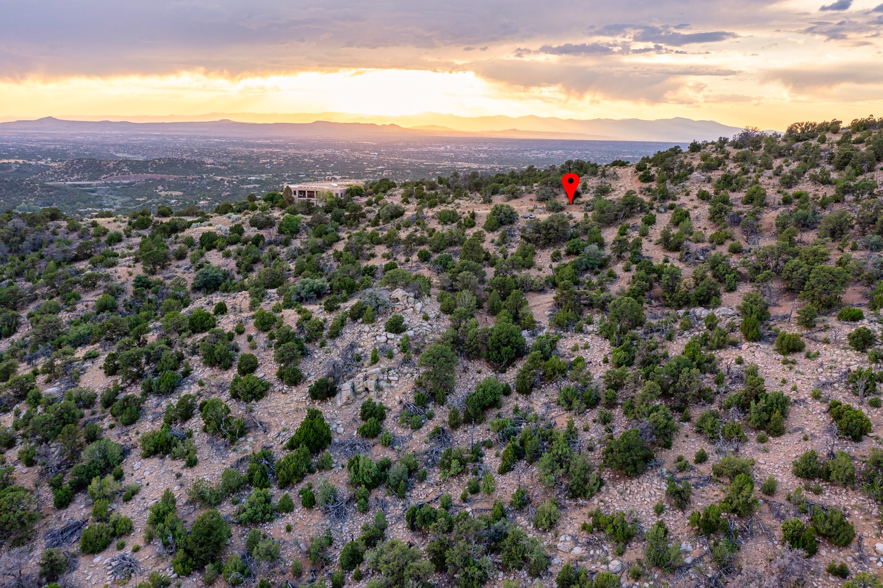 Rocky hillside parcel marked by a red pin, overlooking a valley and distant mountains at sunset.